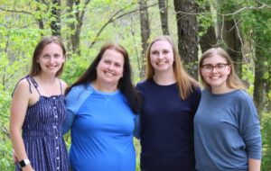 Mother and three daughters wearing blue, stand together in a wooded setting