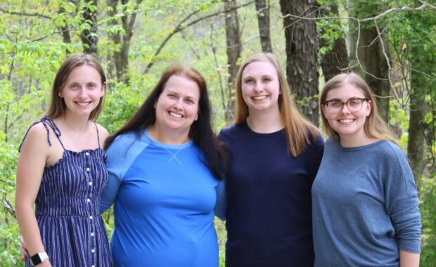 Mother and three daughters wearing blue, stand together in a wooded setting