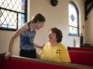 Woman seated in a pew with teenage girl standing next to her