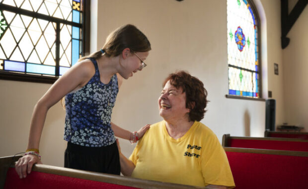 Woman seated in a pew with teenage girl standing next to her