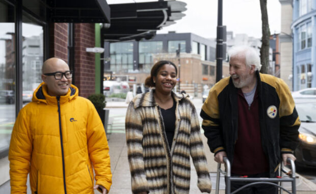 three people walk down a street together. one of them uses a walker