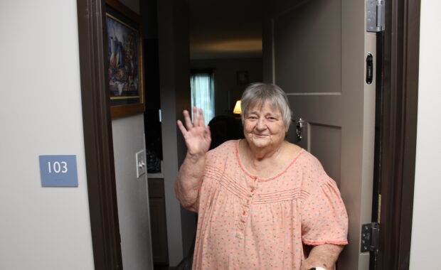 Woman stands in nightgown with walker doorway waving