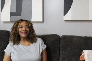 Woman of color sits on couch smiling at camera