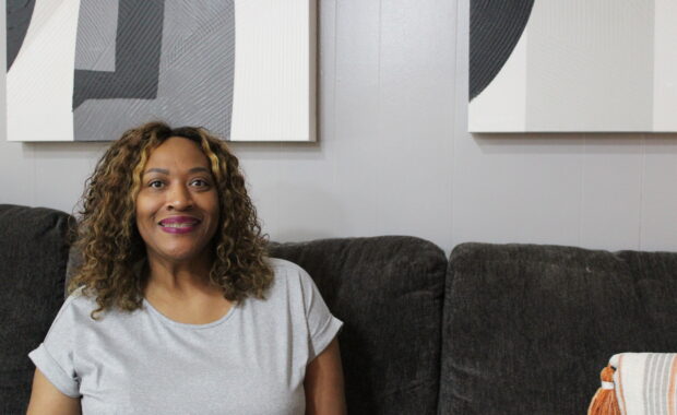 Woman of color sits on couch smiling at camera