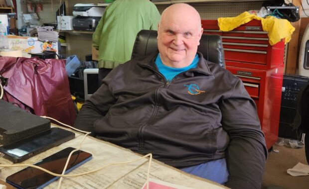 bald man in his 60s sits behind a counter at a thrift store