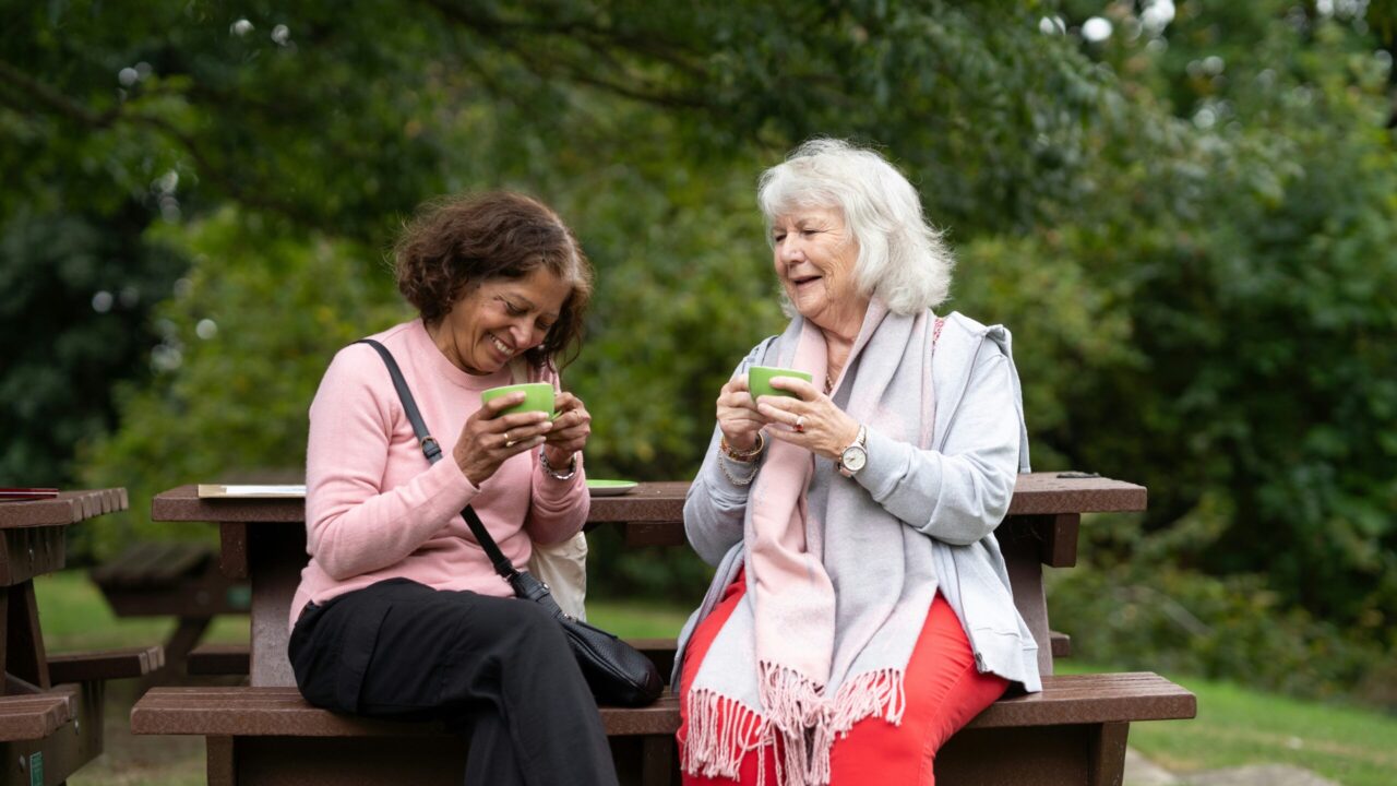 two women enjoy drinks outside on a bench