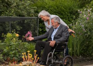 man in wheelchair and woman standing admire flowers