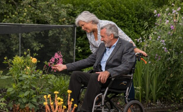 man in wheelchair and woman standing admire flowers