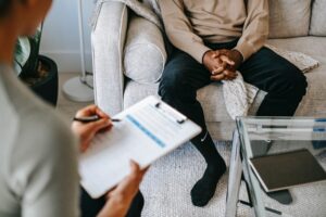 person with clip board sits across from someone on a couch